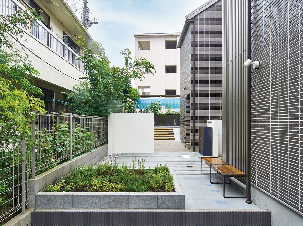敷地奥から入口方面を見る。隣家の緑を借景し、菜園のある共用庭に溶け込ませた。