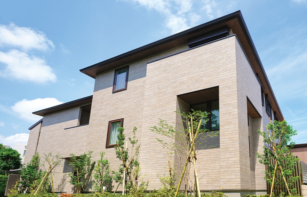 外壁はライトグレーの石材風タイル仕上げ。植栽の緑がよく映える。