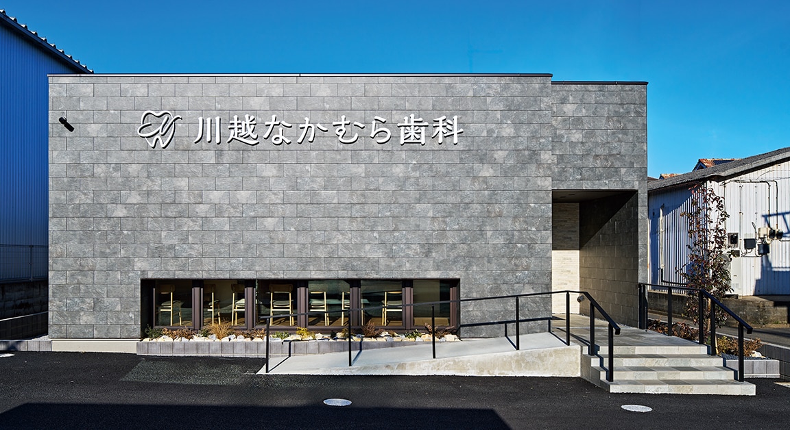 通りに対して端正な表情を見せるファサード。天然石の質感を表現した色ムラのあるシックなタイルが医院の品格を印象づける。階段とスロープを二方向に振り分けた設計が、幅広い世代の来院しやすさにつながっている。