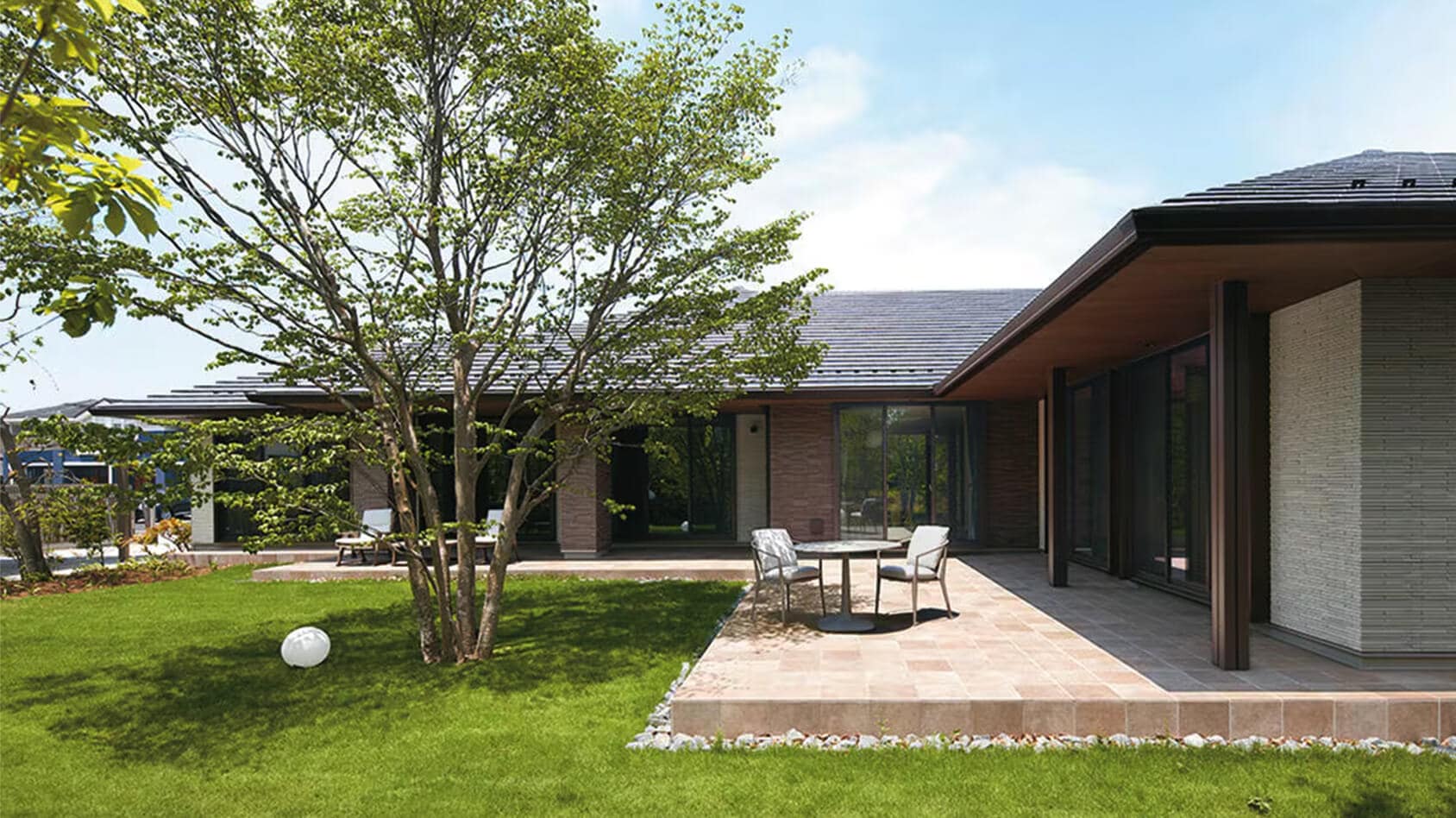 雑木林のような庭園を眺めて、ご夫婦で憩うリゾート感漂う平屋の落ち着きある邸宅の様子